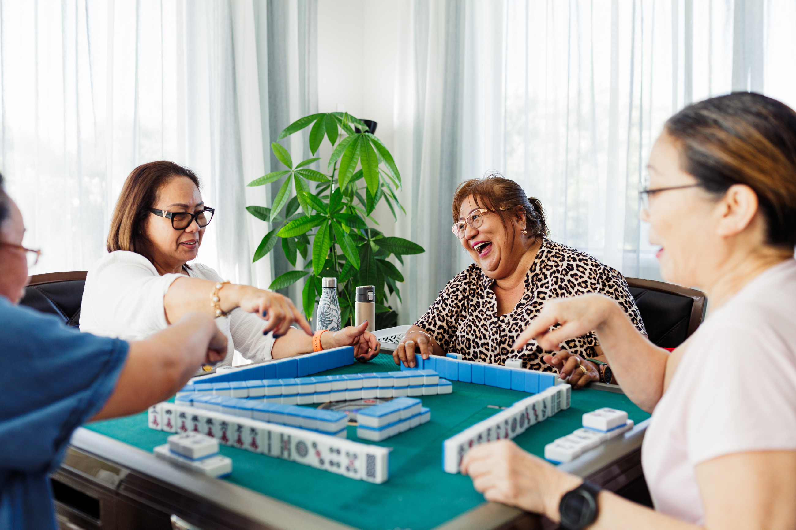 Four people sharing a joyous moment while playing mahjong in a sunlight living room.