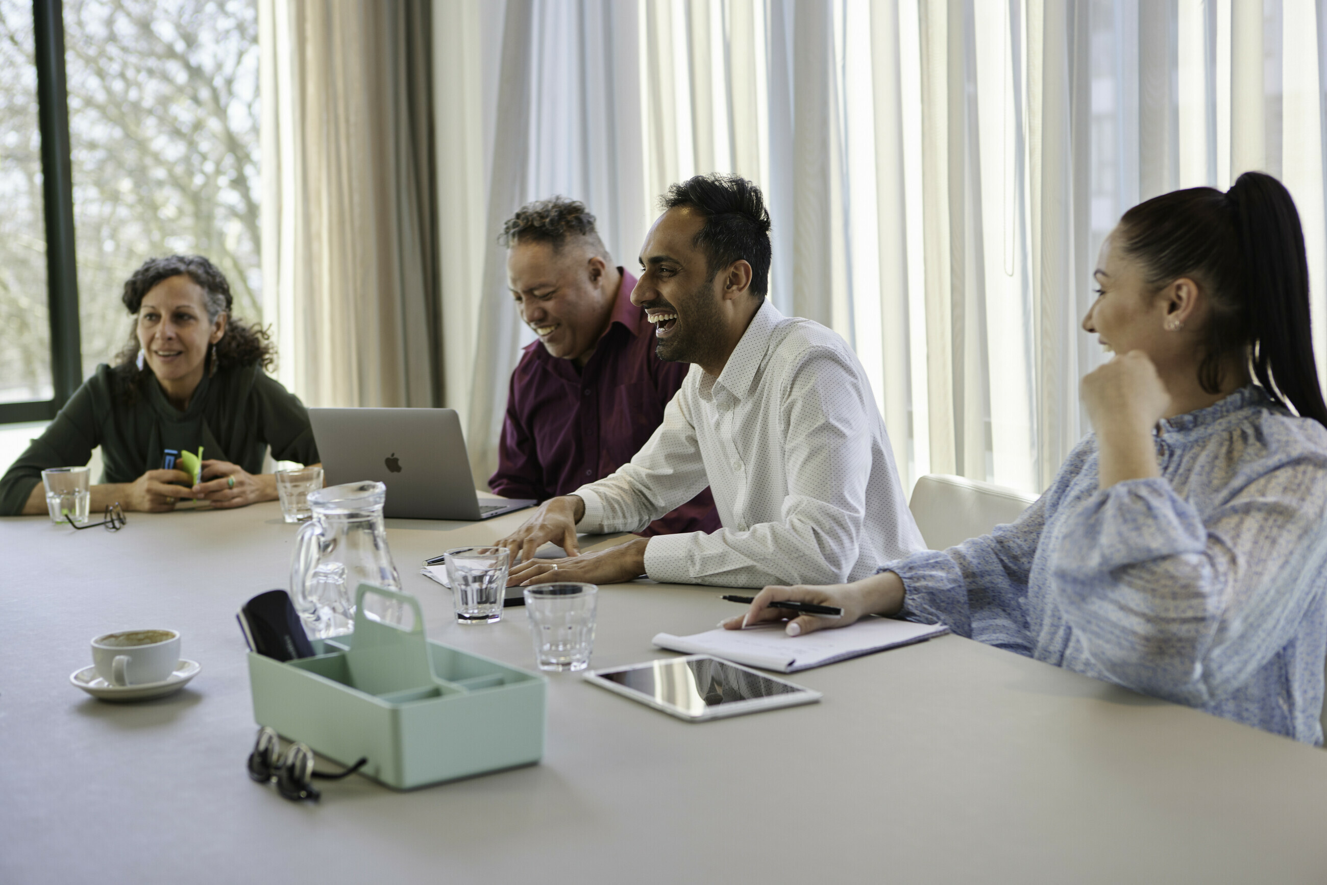 Four people sat around a conference table with their laptops, sharing a happy moment.